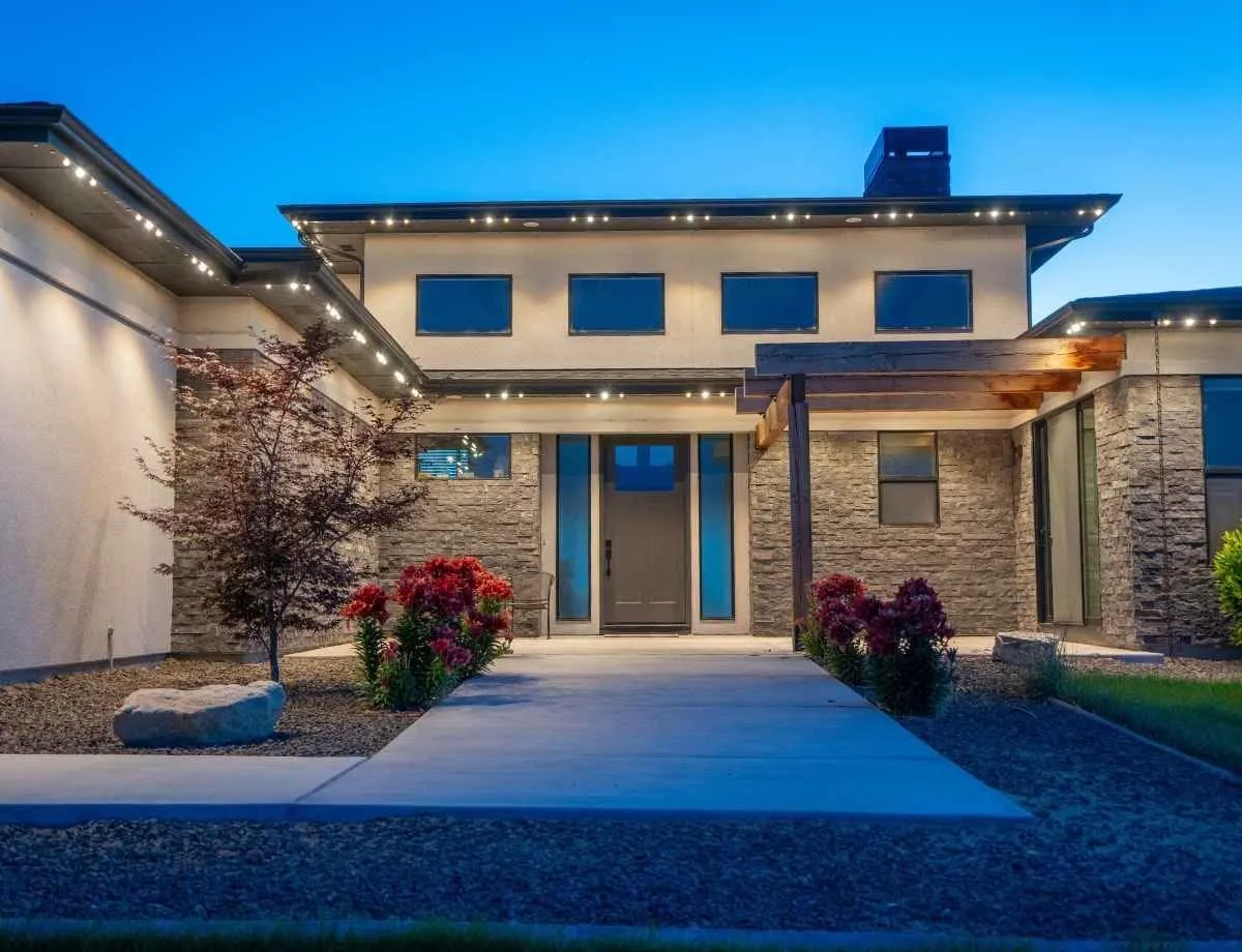 Modern two story home at dusk with warm white lights running along the flat roofline and entry overhang.