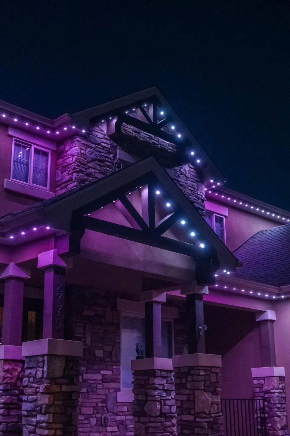 Close view of stacked gables and stone columns lit with purple and white roofline lights at night.